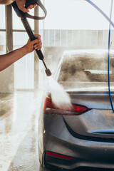 A man washes his car at a self-service car wash using a hose with pressurized water