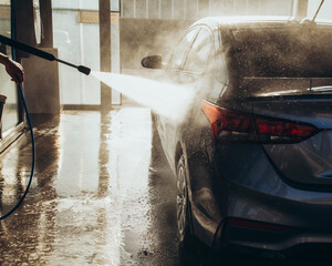 A man washes his car at a self-service car wash using a hose with pressurized water