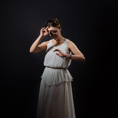An ancient heroine, a young woman in the image of an ancient Greek goddess or muse. A noble heroine in a white tunic and a laurel wreath, a full-length photo on a black background