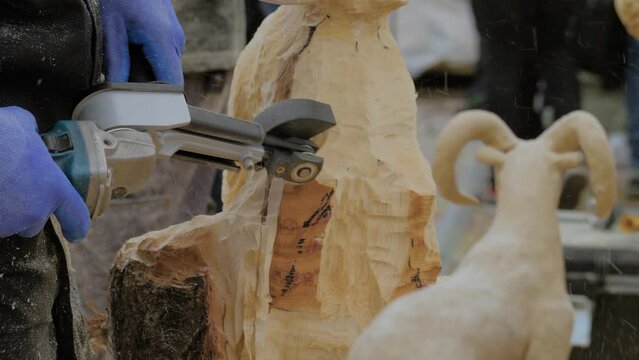 Man carpenter, wood sculptor using angle grinder with multi cutter disk saw attachment for carving wooden sculpture with shavings - close up. Craftsmanship, carpentry, hobby and woodworking concept