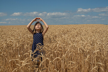 A Ukrainian girl folded her hands in the shape of a heart and prays to God for peace in a wheat field.
