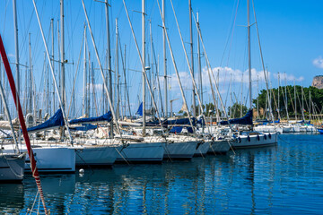 Obraz premium boats and yachts on pier in marine city port with masts and bulidings and blue sky on background