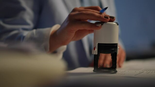 Unrecognizable businesswoman stamping signing documents in office indoors. Close-up round seal in female hand. Successful confident Caucasian woman working with paperwork