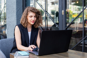 young pretty curly haired business woman using laptop and making video call working remote in cafe