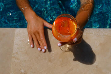 Woman holding aperol spritz cocktail on summer party by the pool. Event celebration concept.