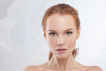 A young attractive red-haired woman with clear skin, a delicate portrait on a light gray...