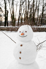 Old sloppy tall snowman with nose made of carrot, buttons made of walnuts stands alone in open...