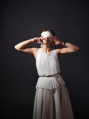 Close your eyes, hide from the truth, concept. An ancient heroine blindfolded, a young woman in a tunic with a blindfold, covers her face with her hands