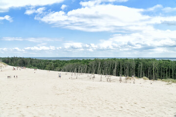 View on Lebsko Lake from Lacka dune in Slowinski National Park in Poland. Traveling dune in sunny summer day. Sandy beach and blue sky with white clouds.
