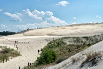 People explore in Lacka dune in Slowinski National Park in Poland. Traveling dune in sunny summer day. Sandy beach and blue sky with white clouds.
