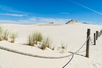 Sandy dunes overgrown by clumps of grass  and blue sky with white clouds in sunny summer day. ...
