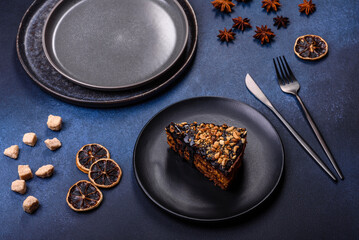 A piece of fresh delicious cake with nuts and chocolate on a black plate against a dark blue background