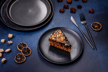 A piece of fresh delicious cake with nuts and chocolate on a black plate against a dark blue background
