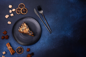A piece of fresh delicious cake with nuts and chocolate on a black plate against a dark blue background