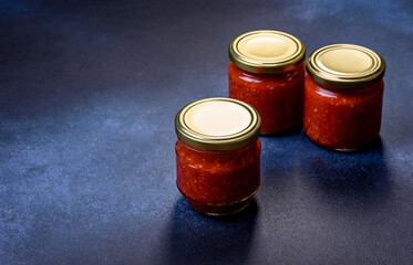 Homemade hot tomato sauce adjika in jars. Tomatoes, chilli pepper, garlic and herbs