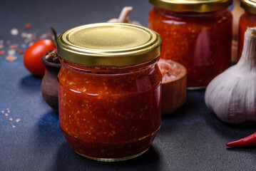 Homemade hot tomato sauce adjika in jars. Tomatoes, chilli pepper, garlic and herbs