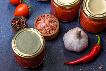 Homemade hot tomato sauce adjika in jars. Tomatoes, chilli pepper, garlic and herbs