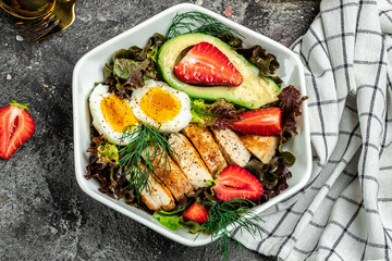 Healthy nutritious paleo keto breakfast diet two eggs, avocado, grilled chicken fillet, nuts, strawberries and fresh salad. Keto breakfast or lunch. place for text, top view