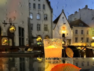  glass cup with candle light on table on medieval street evening blurred bokeh light under rain drops on window in Tallinn old town Autumn holiday in Estonia
