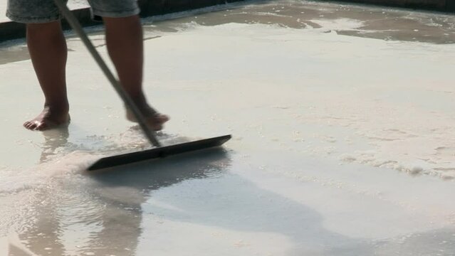 Image of bare feet and legs of a man working in the salt pans adding salt with a wooden shovel