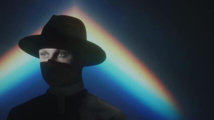 Chest up tracking shot of man in Catholic priest outfit with window blinds shadow on his face posing in dark studio with rainbow light projection