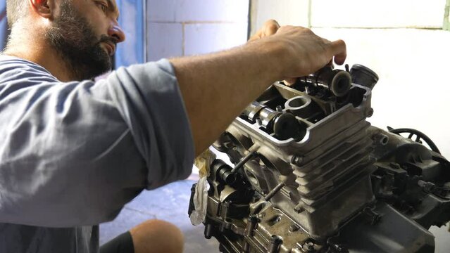 Professional mechanic repairing motor from some vehicle. Auto master fixing motorcycle engine in garage or workshop. Bearded man engaged servicing cars or motorbikes. Close up Slow motion