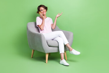 Fototapeta na wymiar Photo of positive lady stylish clothes sit cozy chair look empty space friends telephone conversation 5g isolated on green color background