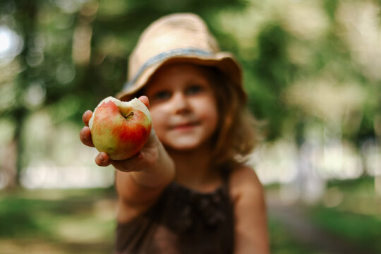Portrait of a child with an apple in his hands. Baby 5 years old eats an apple. Girl in a straw hat.