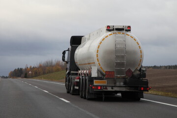 Petrol transportation, white fuel tank truck with ADR sign 33 1203 on suburban empty asphalted road at autumn evening on gray sky background, flammable liquid goods transportation - obrazy, fototapety, plakaty
