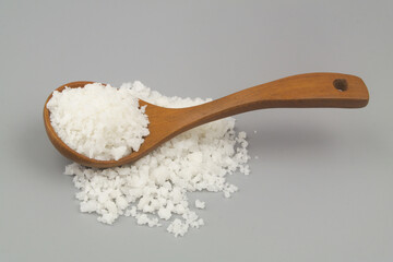 Salt in wooden spoon and on gray background