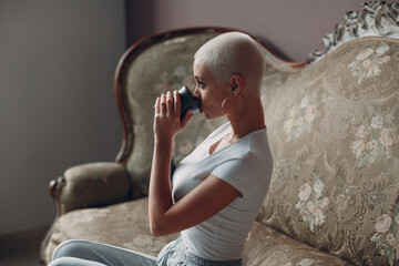Millenial young woman with short blonde hair portrait sitting with cup of tea or coffee drink on...