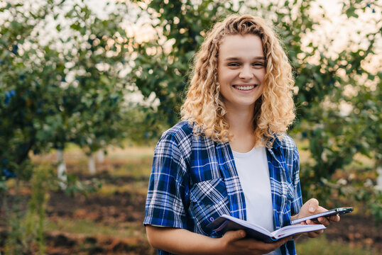 The agricultural expert smiling at the camera happy that she has finished examining the plum trees, holding a notebook in which she writes down her observations