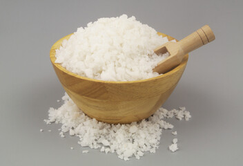 Wooden bowl with coarse salt and wooden scoop on gray background.	
