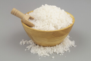 Wooden bowl with salt and scoop on gray background.	