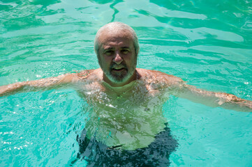 retired man swimming in summer pool on summertime vacation