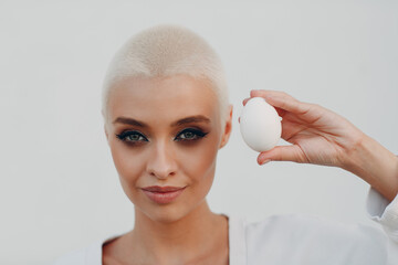 Portrait of young smiling millenial european short haired woman hold egg in hand. Beautiful happy...