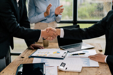 Close up of female and male shaking hands, businessman and businesswoman handshaking at office table with charts graphs after successful negotiations, partners concluding contract