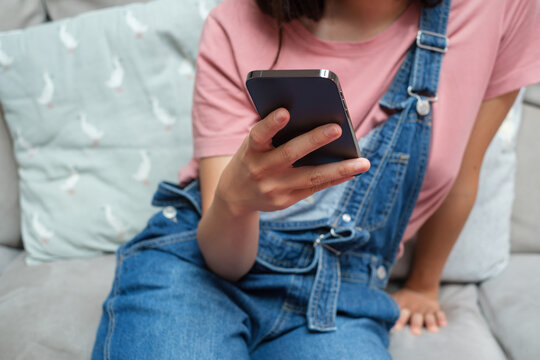 Cropped Image Of Woman with Bib Overalls using phone on coach