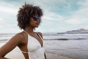 Portrait of beautiful black woman with curly hair wearing sunglasses on the beach.