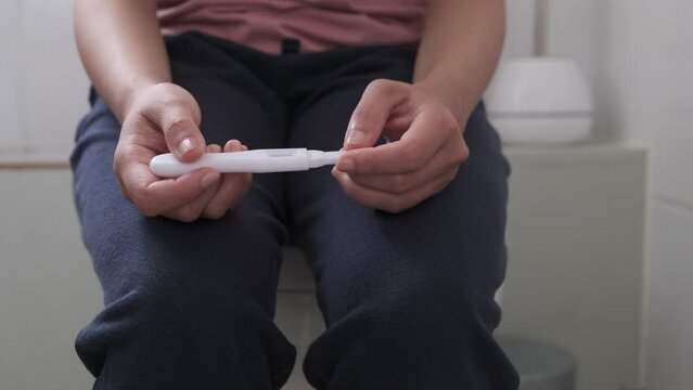 Cropped Image Of Woman Sitting In Toilet and Holding Pregnancy Kit