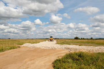 Road construction. Bulldozer paves way. Road works in green field. Bulldozer drives off into distance on gravel. Laying roads in countryside. Special construction machinery in field.