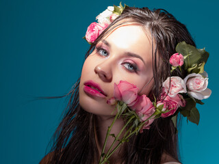 A young beautiful woman with rose flowers in her wet hair. Portrait of a beautiful brunette with perfect skin, close-up on a blue background