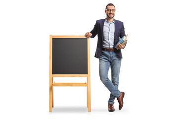 Full length portrait of a male teacher holding books and standing next to a blackboard on a stand