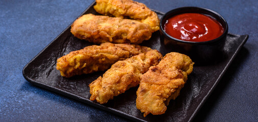 Fried crispy chicken nuggets with ketchup on black plate on a dark background