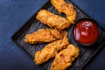 Fried crispy chicken nuggets with ketchup on black plate on a dark background