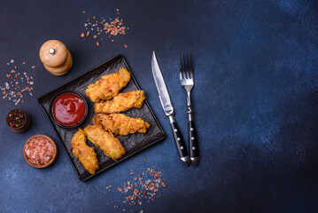 Fried crispy chicken nuggets with ketchup on black plate on a dark background