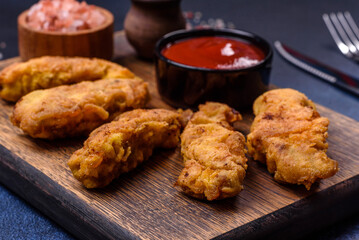 Fried crispy chicken nuggets with ketchup on black plate on a dark background