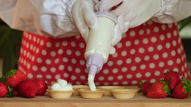 Chef sprinkling sugar powder on tasty mini cake with cream and strawberries, slow motion. Powdered sugar being sieved on strawberry tart. Dessert dusted with castor sugar