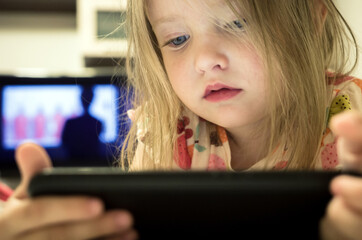 Small baby girl looking on smartphone and television. Mobile phone addiction in kid concept