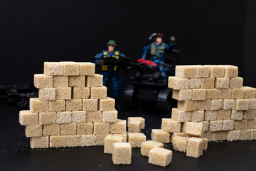 Defocused toy police men,  tearing down a wall made from brown sugar cubes